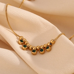Close-up of gold stainless steel box chain anklet with green zircon and round gold beads