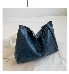 Detail view of large blue tote bag with oily leather texture on soft white fabric