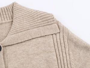 Detailed close-up of ribbed shawl collar and black button on beige knit cardigan sweater