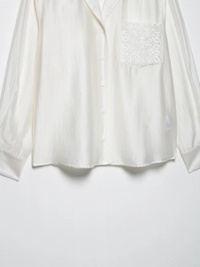 Detailed macro view of the glossy satin fabric and embroidery on the white shirt pocket