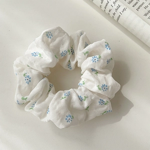 Detailed close-up of a white floral hair scrunchie with blue patterns on a textured desk