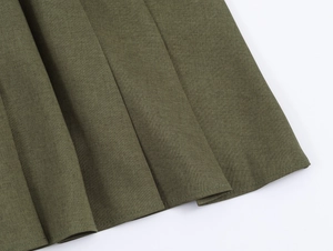 Détail de l'ourlet de la jupe plissée vert olive montrant le tissu tissé texturé