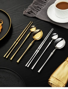 Polished silver and gold stainless steel cutlery set on a black wood dining table