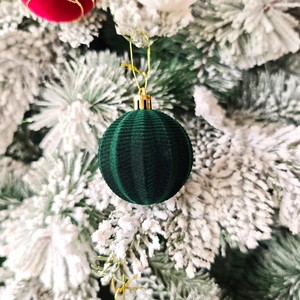 Boule de Noël en velours vert à côtes suspendue sur une branche de sapin enneigée
