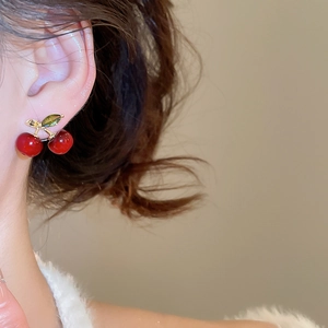 Macro side view of cherry earrings with red resin spheres and gold leaves on a model