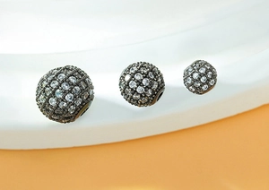 Macro shot of three sizes of black pave zircon ball charms on a white wavy display stand