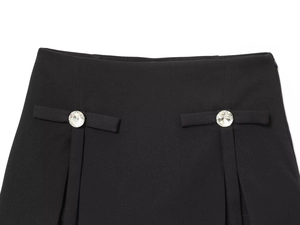 Detailed close-up of black skirt waist with sparkling rhinestone buttons and pleated accents