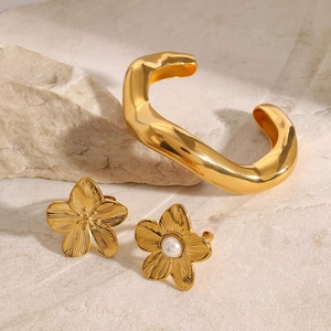 Gold plated cuff bracelet and flower earrings set with pearl on elegant stone background