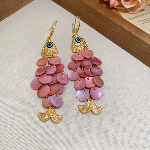 Detailed close-up of fish-shaped shell earrings with pink scales and blue evil eye details
