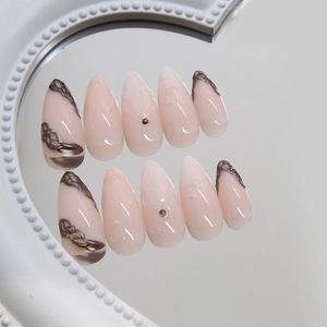 Almond-shaped nude pink press-on nails with 3D swirl patterns and small bead accents