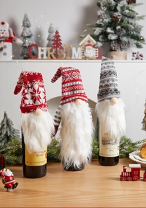 Close-up of three knitted Christmas gnome wine bottle covers with snowflakes and stripes