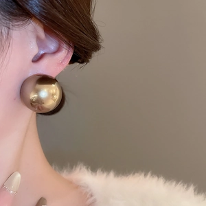 Gros plan d'une grande boucle d'oreille sphérique dorée avec finition miroir sur le mannequin