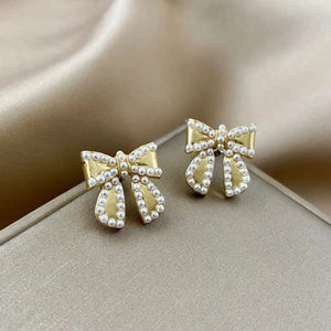 Detail of elegant gold bow earrings with white pearls on champagne satin background