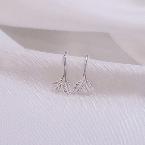 Macro shot of silver leaf earrings showing detailed veins on white fabric background