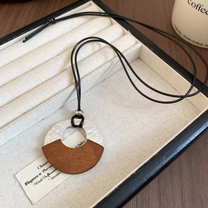 Detail of silver hammered metal and dark wood pendant on black cord necklace