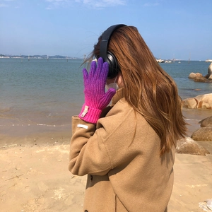 Rainbow gradient knitted touch-screen gloves worn by model at the beach scenery