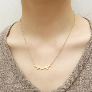 Detailed close-up of golden swallow bird pendant necklace worn by a model