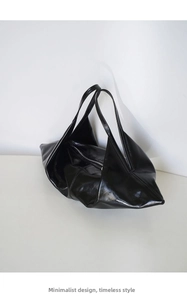 Detailed close-up of glossy black leather hobo bag featuring a minimalist fold design