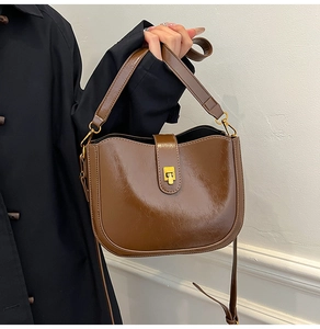 Detail of coffee brown retro saddle bag with glossy texture and gold metal buckle