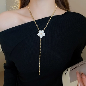 Fashion long gold bead necklace featuring a white flower pendant on a black knit sweater