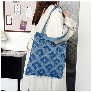 Blue denim tote bag with star patterns and frayed edges shown on a model's shoulder