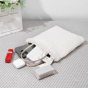 White plush faux fur handbag with daily essentials shown on a cozy knit background