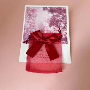 Detail of red organza gift bag with ribbon bow on pink background with cherry blossoms
