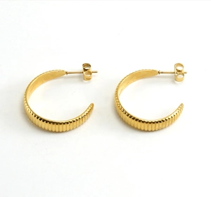 Détail de boucles d'oreilles dorées en C avec rayures verticales et fini brillant