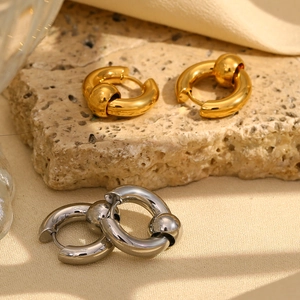 Macro detail of gold and silver beaded hoop earrings on minimalist textured surfaces