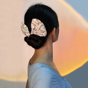 Détail d'un accessoire chignon avec nœud à motif floral rose sur tissu crème