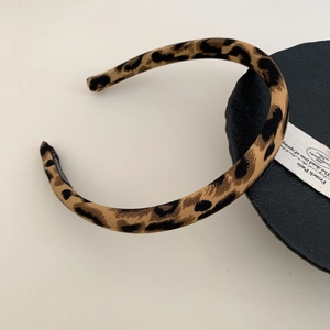Detail view of leopard print thin headband with protective black tips on dark circular base