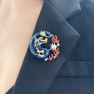 Detailed close-up of a blue and gold Chinese dragon brooch with white pearl on a black suit