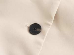 Macro view of beige twill fabric texture and black four-hole button detail on the suit