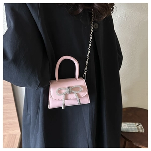 Pink mini crossbody bag with rhinestone bow and silver chain strap on black coat