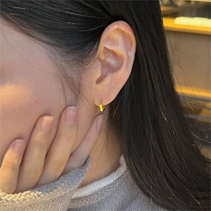Close-up of minimalist rectangular gold hoop earring worn on an earlobe in a warm setting