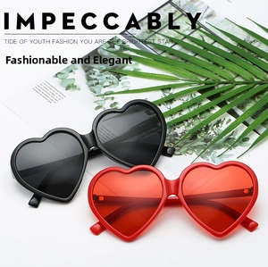 Flat lay of red and black heart-shaped sunglasses with metallic hinges on palm leaf background