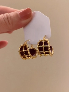Detail of vintage gold-plated cage earrings with premium dark leather inlay texture