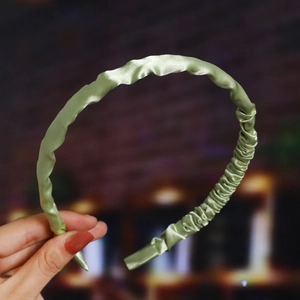 Close-up of light green pleated satin headband with a glossy finish and elegant texture