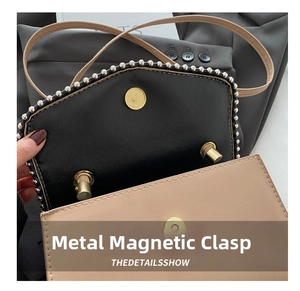 Detailed close-up of metal magnetic buckle and pearl trim on contrast shoulder bag
