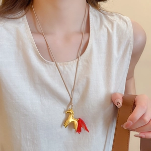 Close-up of golden horse pendant necklace with red beaded tail on a female model