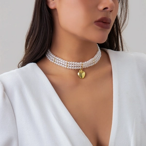 Close-up of triple-layer pearl choker with a polished gold heart pendant on a model
