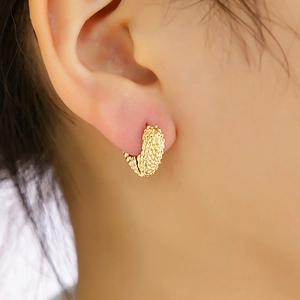 Détail de la boucle d'oreille dorée à texture tressée sur le lobe de l'oreille
