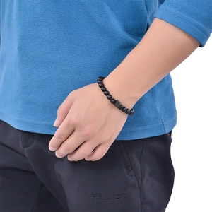 Detailed view of men's matte black lava stone bracelet with engraved square charm on wrist