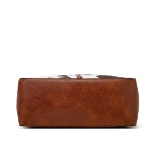 Detail view of the brown textured leather base and cow print pattern of the tote bag