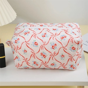 Detail of a white quilted makeup bag featuring red bows and blue floral patterns