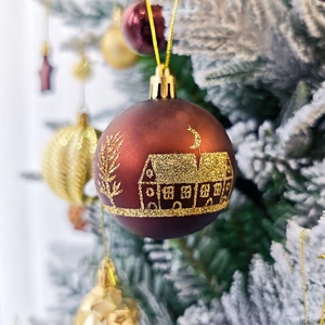 Gros plan sur une boule de Noël rouge foncé avec motif de maison dorée sur sapin