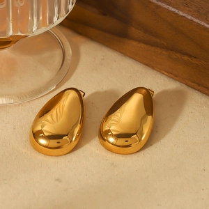 Macro detail of high-polish gold teardrop earrings on a minimalist textured backdrop