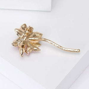 Elegant gold lotus flower brooch with long stem on a minimalist white geometric background