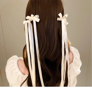Detail of elegant cream satin bow hair clip with long ribbons worn on model hair