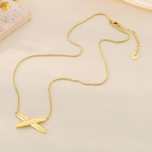 Polished gold X-shape crossover pendant on a delicate chain over beige background